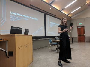 Kelsey standing at the front of a lecture hall, beginning a lecture entitled: Long Term Memory: Learning