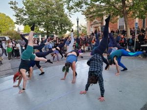 Kelsey and a group of dancers dressed in shades of blue and teal performing an "inversion" in which their hands are on the ground and their legs are in the air.